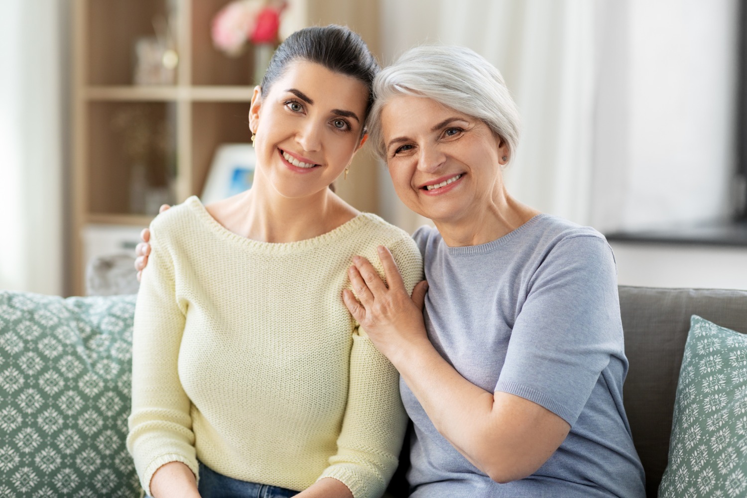 Adult daughter and senior mother smiling on the couch