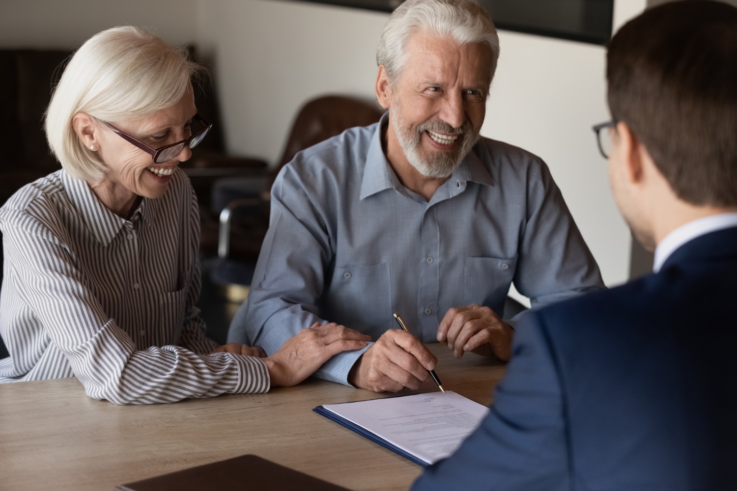 Smiling senior couple signing Medicaid planning documents with an advisor