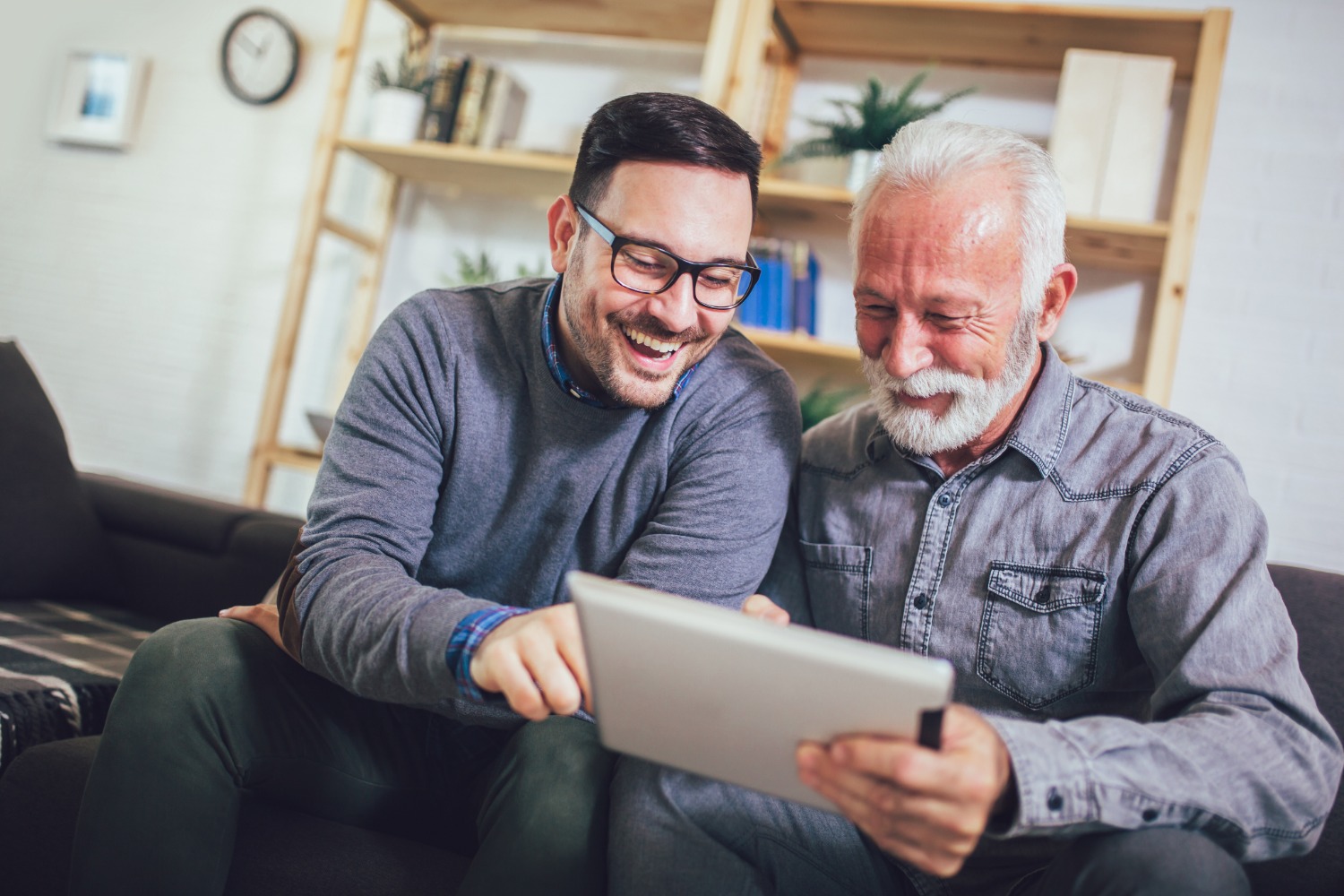 Adult son helping his senior father review information on a tablet