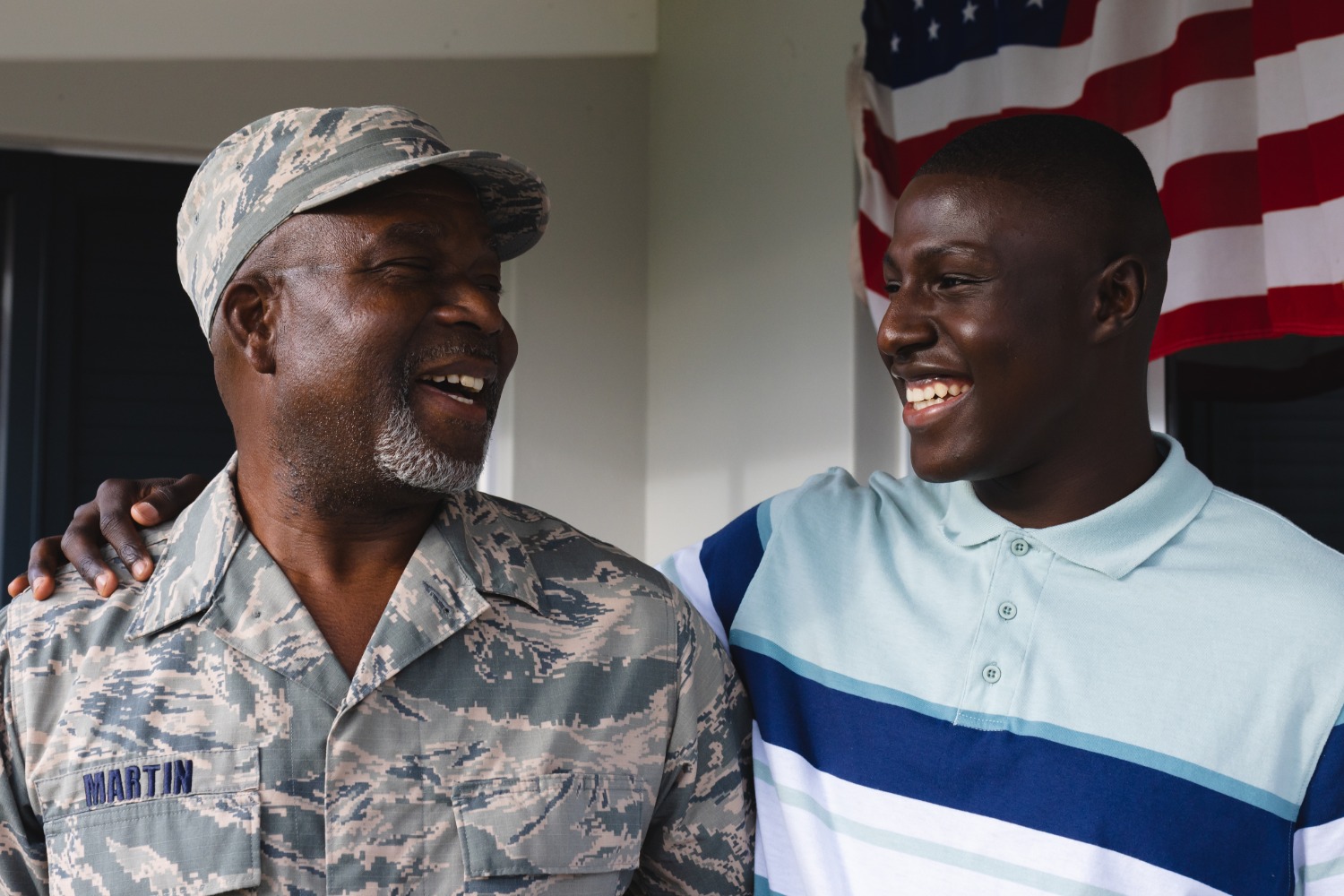 Smiling veteran in uniform with his son in front of an American flag